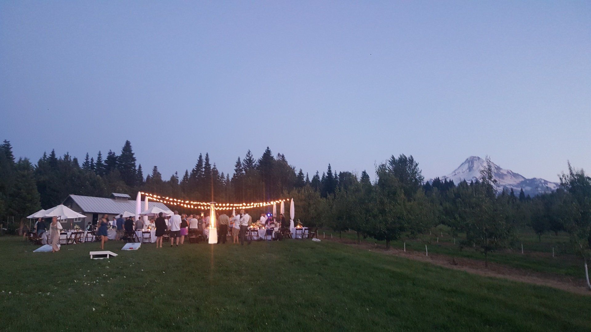 Outdoor evening gathering with lights strung up, mountain in the background.