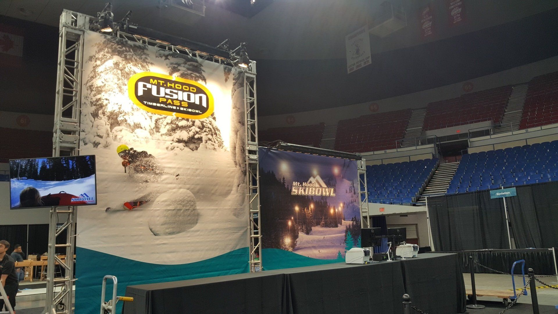 Event stage setup with large banners and screens in an arena. A skier is pictured on a large banner.