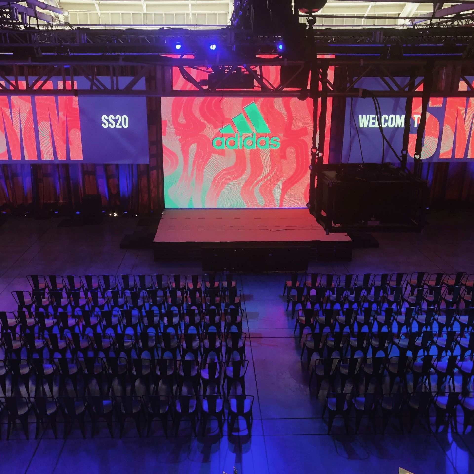Adidas event stage, large screen with logo, seating arrangement, empty chairs, SS20 text,
