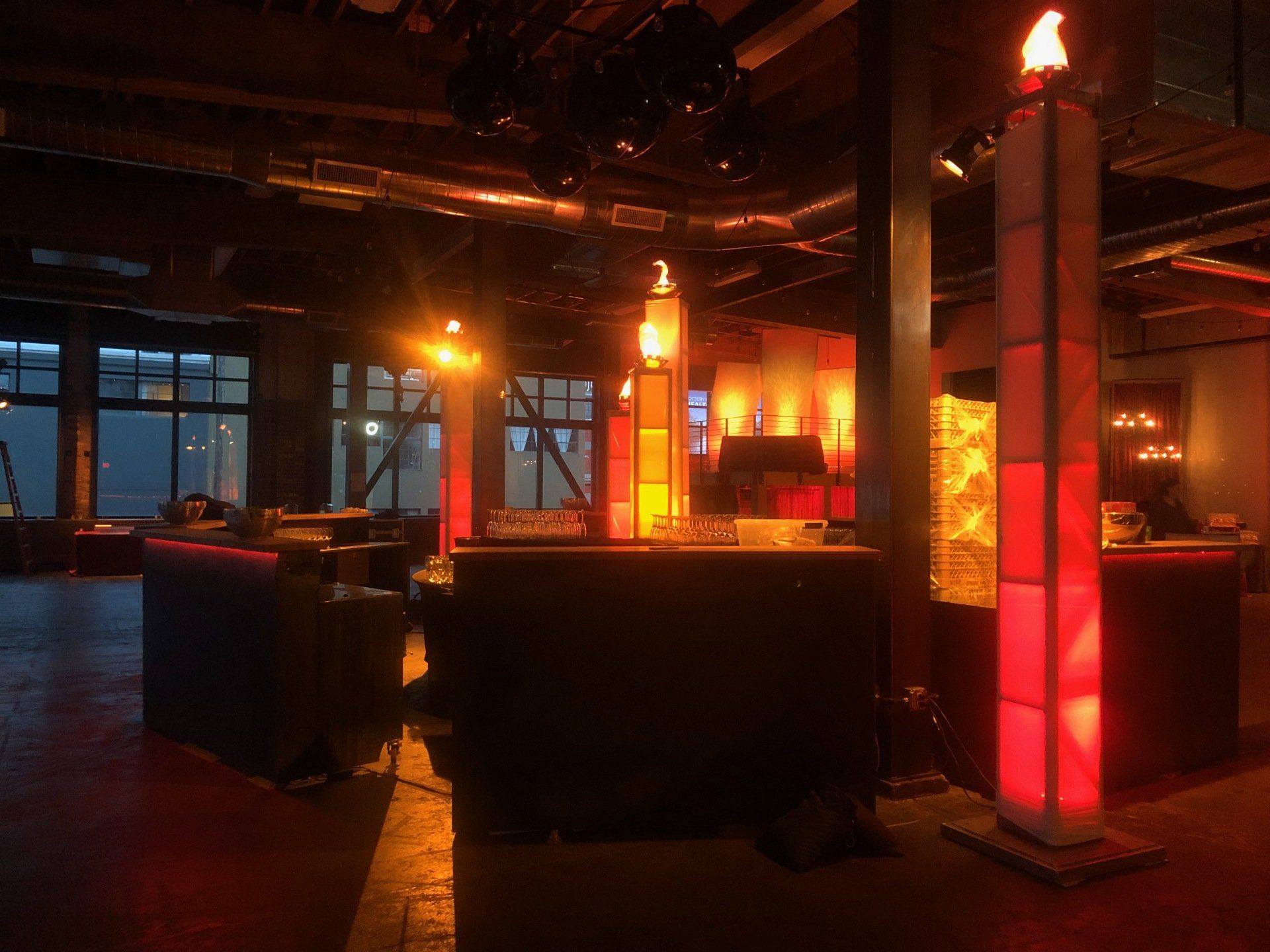 Inside a dimly lit venue with red and orange lighting. DJ booth and decorative flame columns.