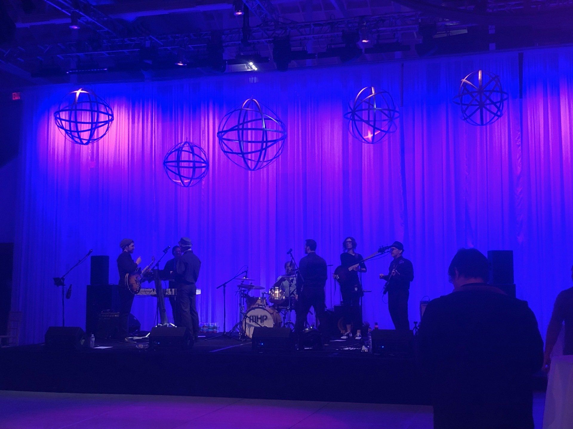 Band performing on stage with blue and pink lighting, decorative orbs.
