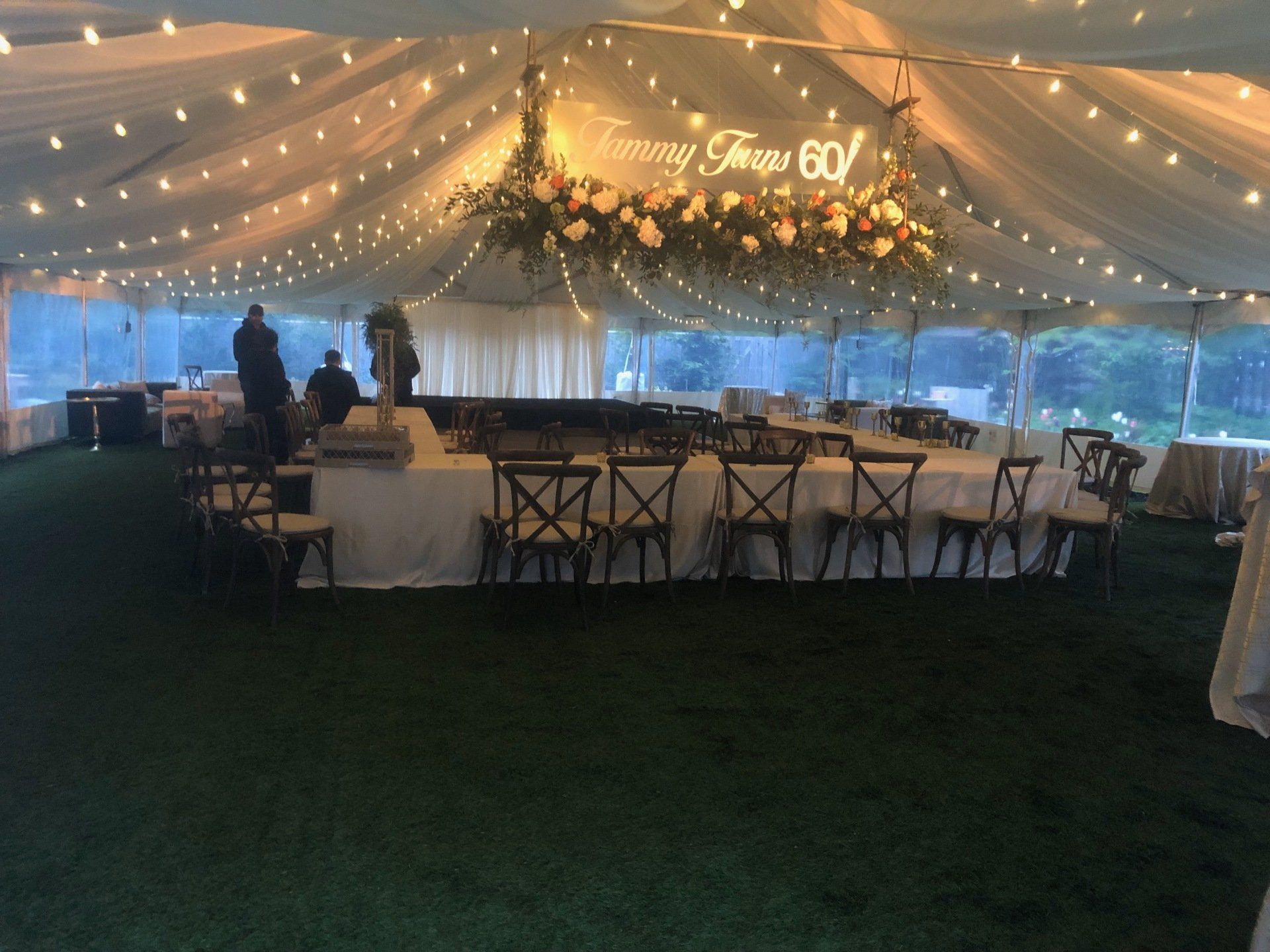 Tent decorated for a celebration, with string lights, floral arrangements, tables, and chairs.