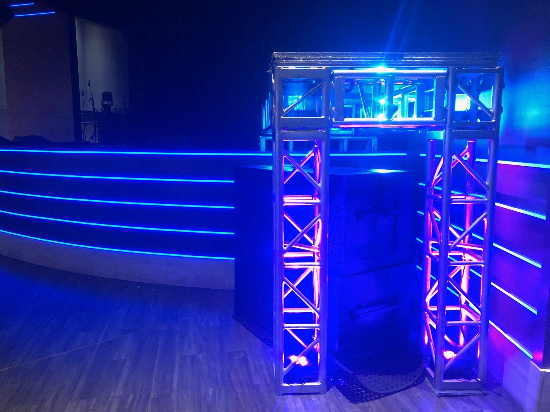 Blue lit stage with a metal truss archway and a dark background.