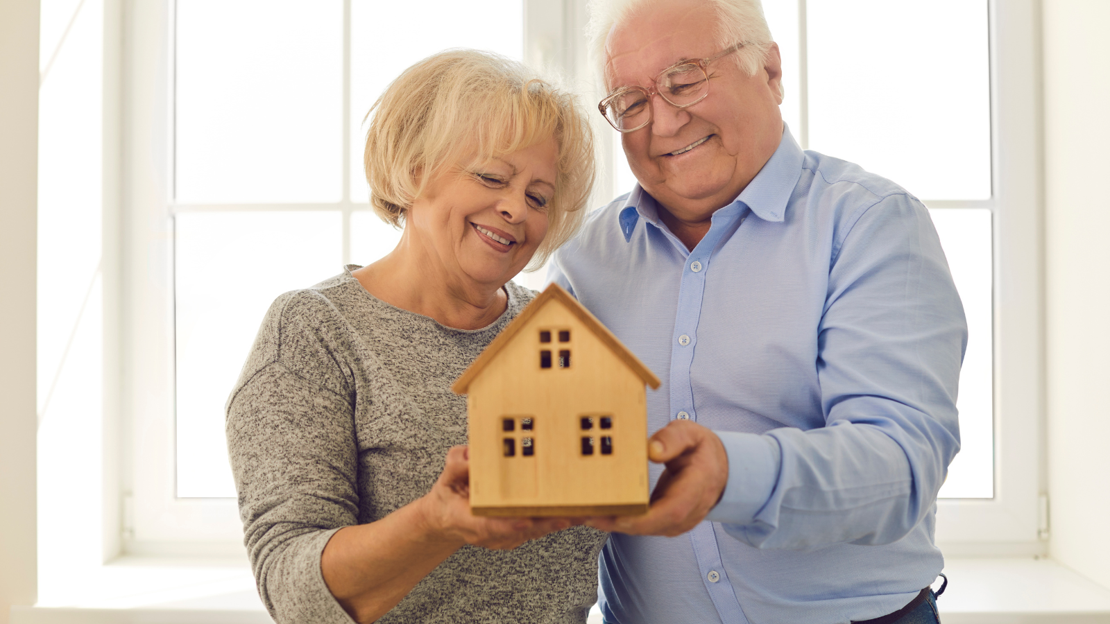 An elderly couple holding a model of a house in thier hands.