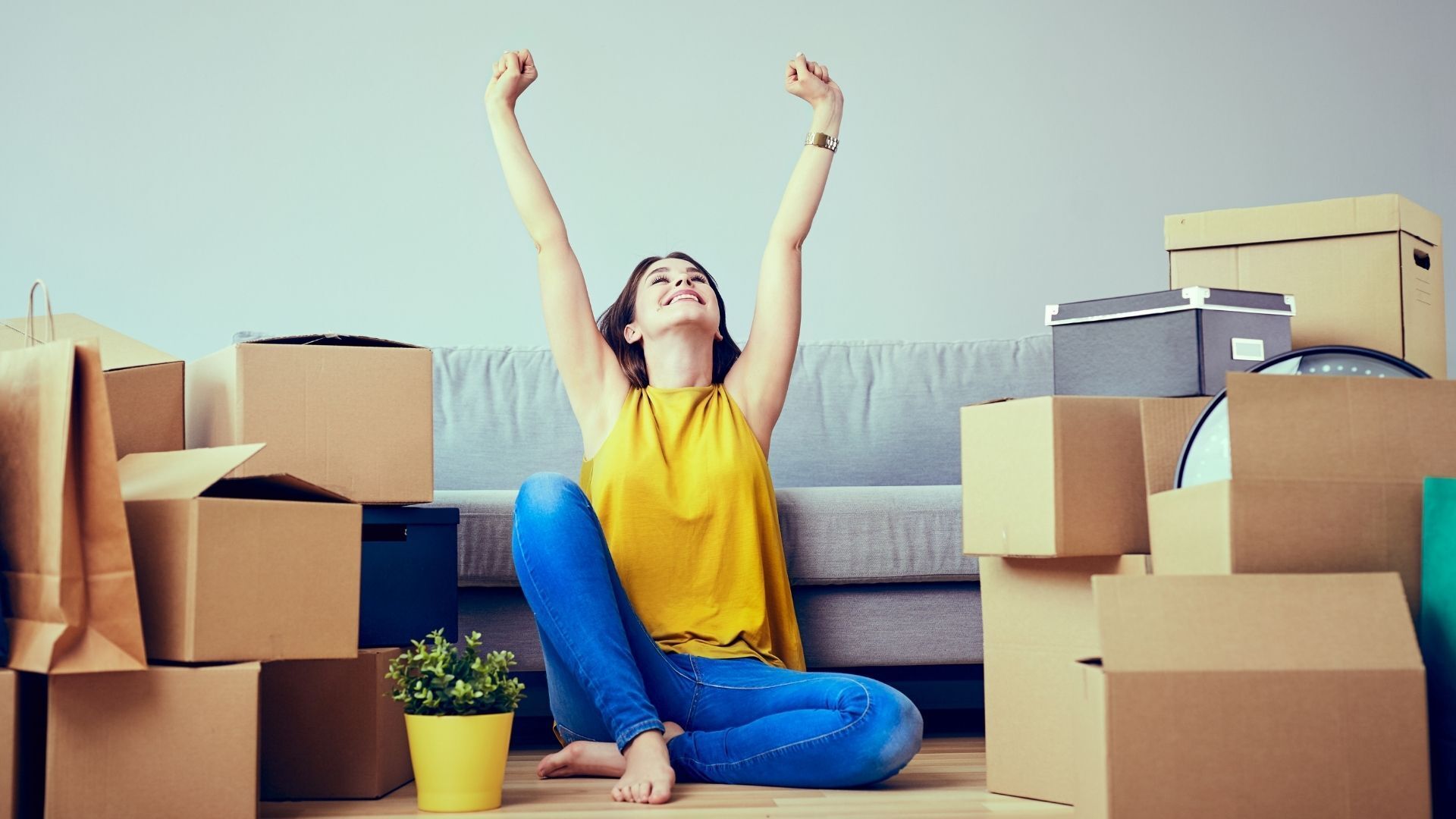 Girl sitting on the floor around multiple moving packages and raising both arms and stretching after