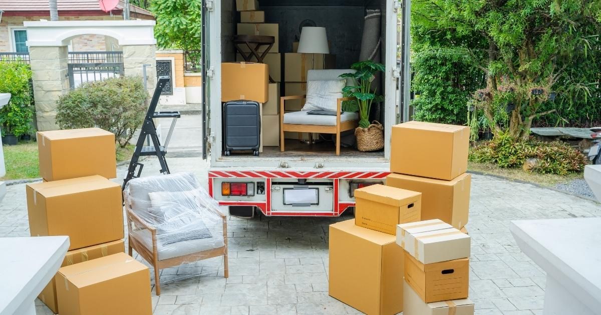 Moving truck open, boxes and furniture on the ground and inside, loading in progress.