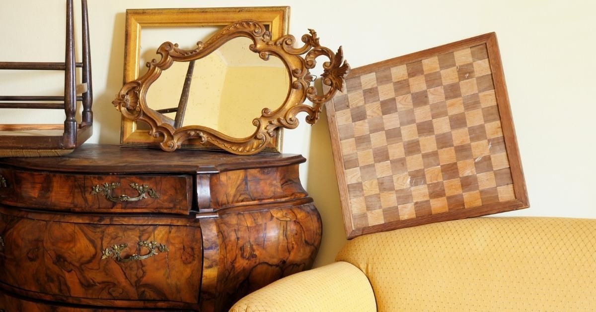 Decorative mirror and checkered pillow on a carved wooden dresser beside a yellow sofa
