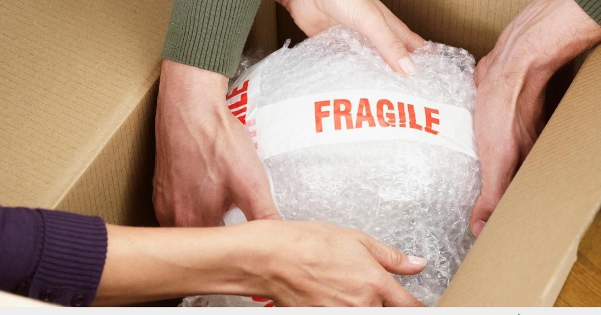 Hands carefully placing a bubble-wrapped item labeled