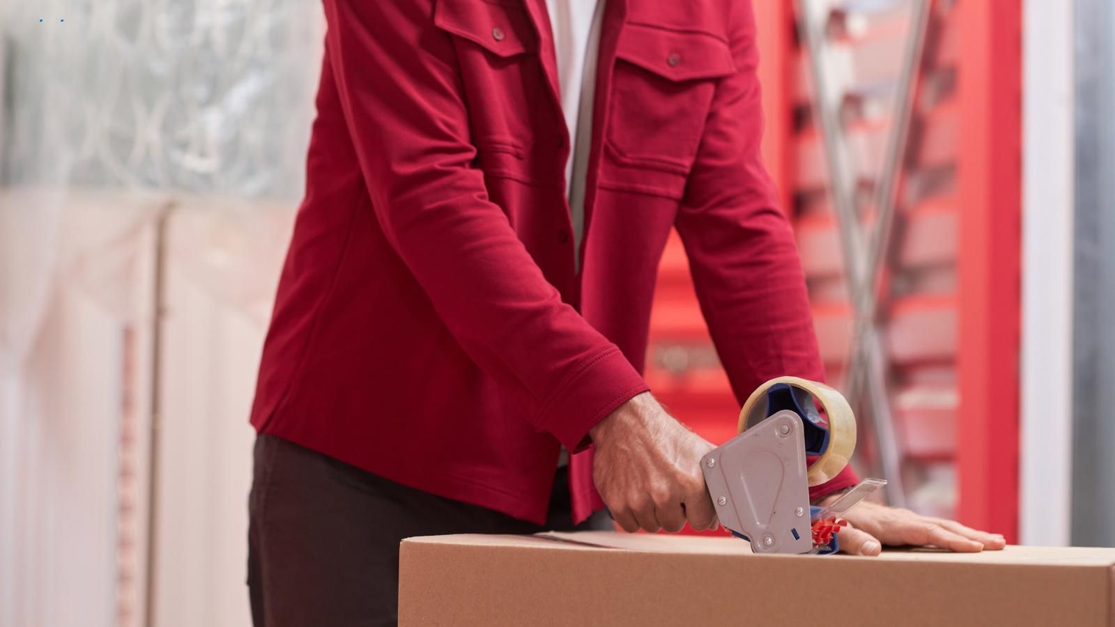 A man in a red jacket taps a cardboard box in a personal self-storage.