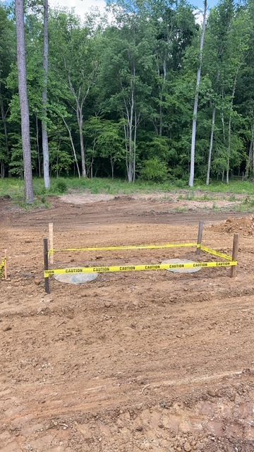 A dirt field with a yellow tape around it and trees in the background.