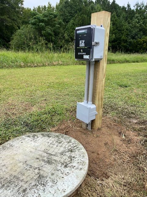 A wooden post with a box attached to it is in the middle of a grassy field.
