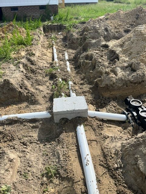 A drainage system is being installed in the dirt in front of a house.