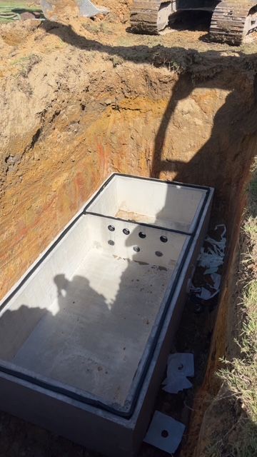 A large concrete box is sitting in the dirt next to a large excavator.