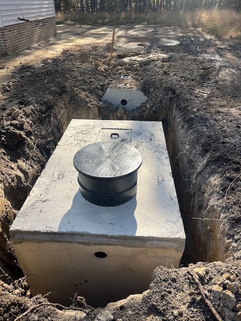 A large concrete septic tank is sitting in the middle of a dirt field.