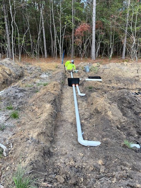 A man is working on a septic system in the dirt in the woods.