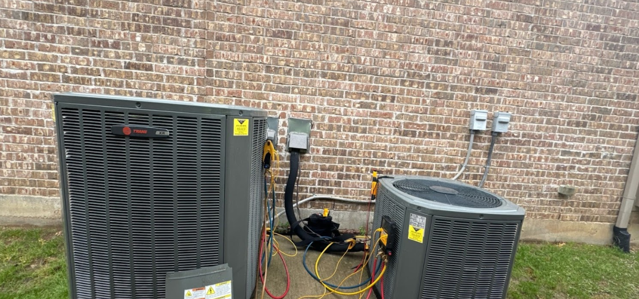 Two air conditioners are sitting next to each other in front of a brick wall.