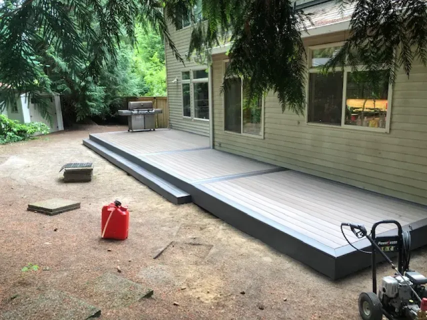 Composite deck attached to a light-colored house. Charcoal gray trim and steps. Red gas can, pressure washer.
