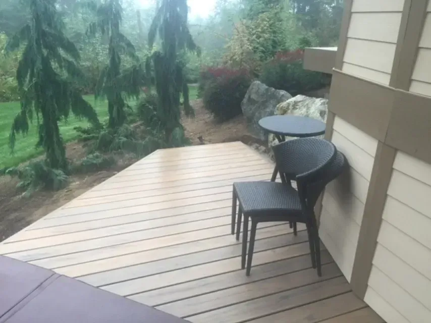 Outdoor wooden deck with a chair, small table, and surrounding greenery.