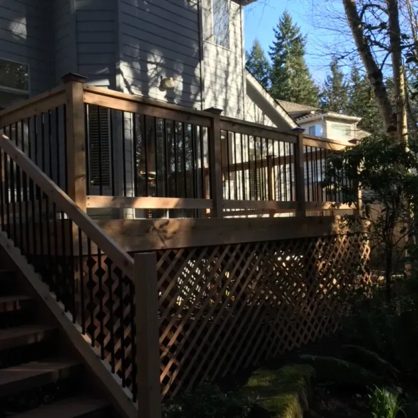 Wooden deck with stairs, lattice skirting, and black railing spindles on a gray house exterior.