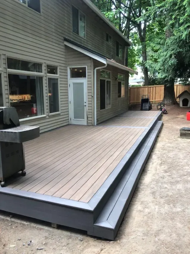 Backyard deck with composite decking and gray trim, next to a two-story beige house and a fence.