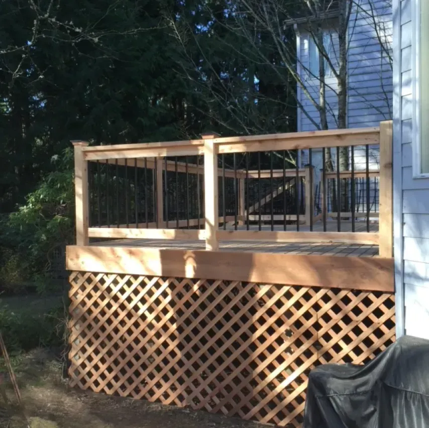 Wooden deck with lattice skirting and black metal railing, next to a light blue house.