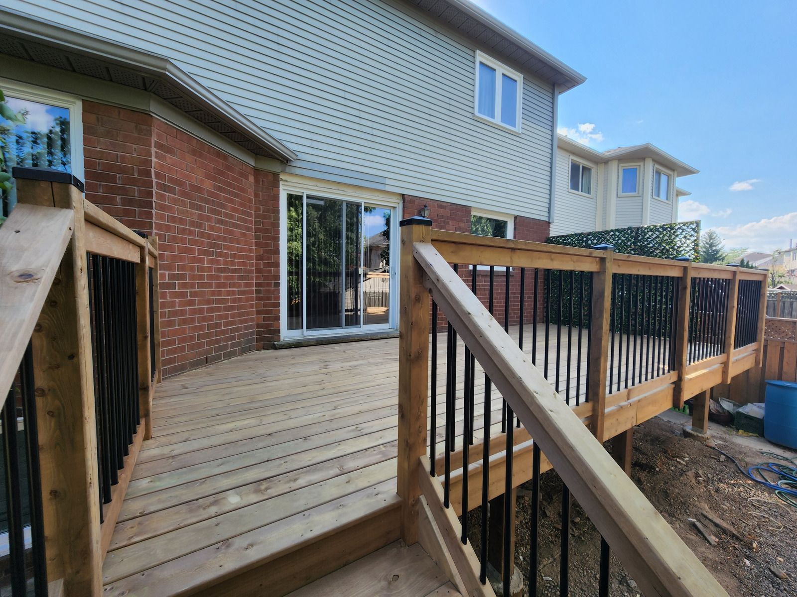 Wooden deck with black railings and a house in the background.