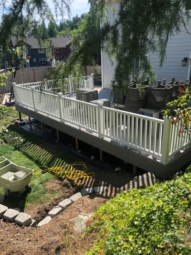 A white-railed deck overlooks a sloped backyard with a rock retaining wall and surrounding greenery.
