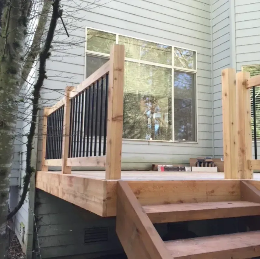Wooden deck with black railings and stairs in front of a light-colored house.