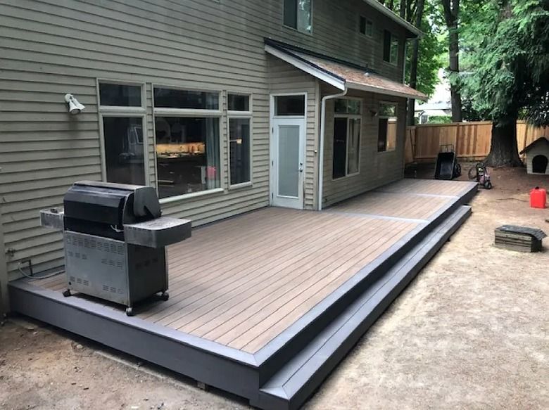 Backyard deck with a grill and access to a two-story house.