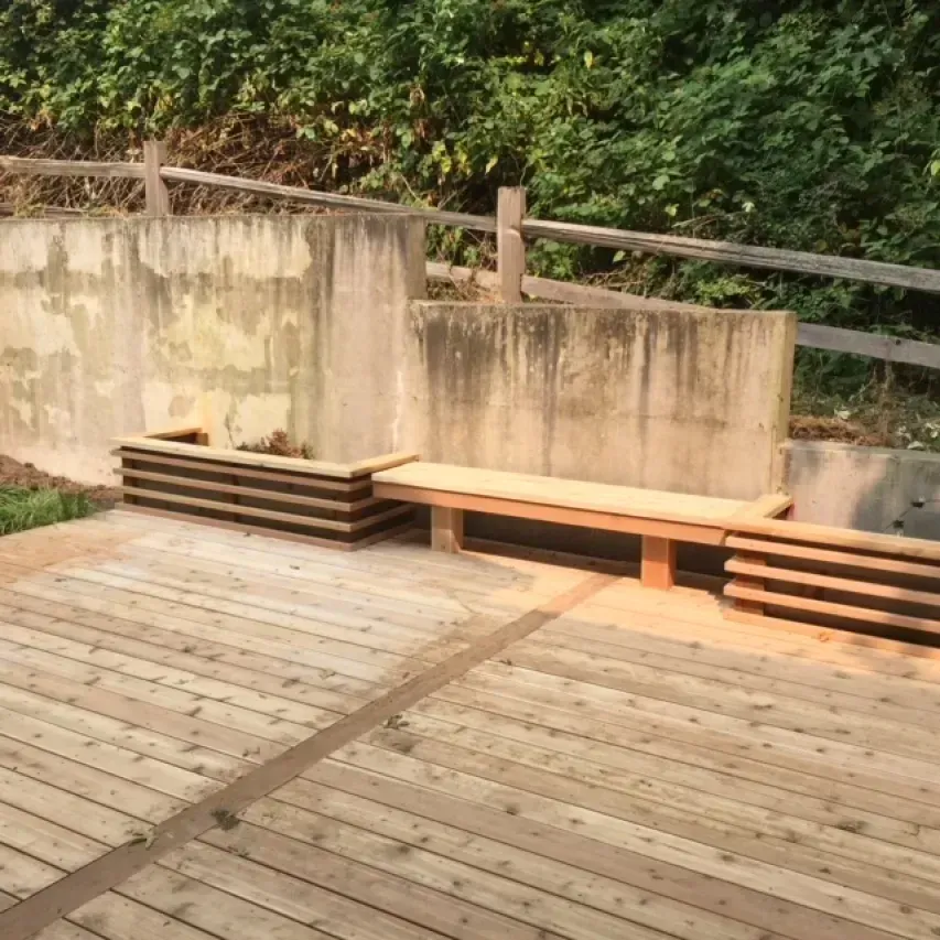 Wooden deck with concrete wall and bench, surrounded by greenery.