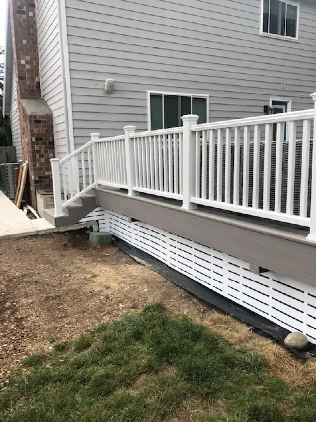 White deck with stairs, railing, and skirting attached to a gray house.