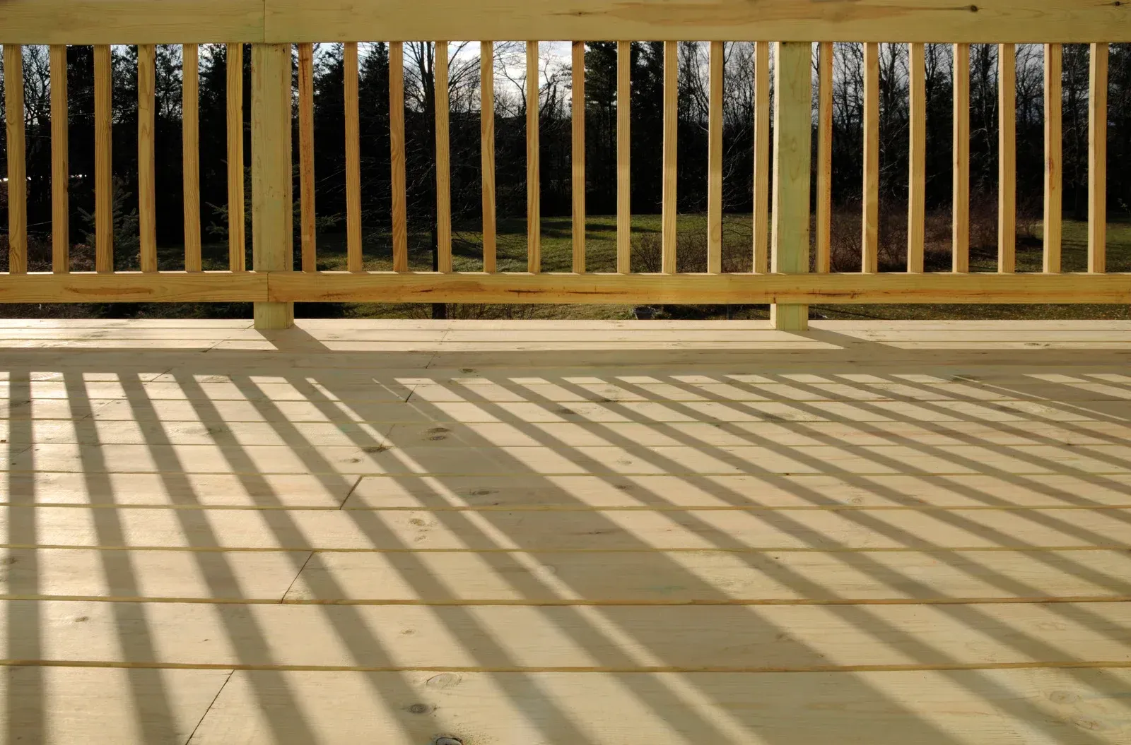 Wooden deck with railing casting long shadows on the planks.