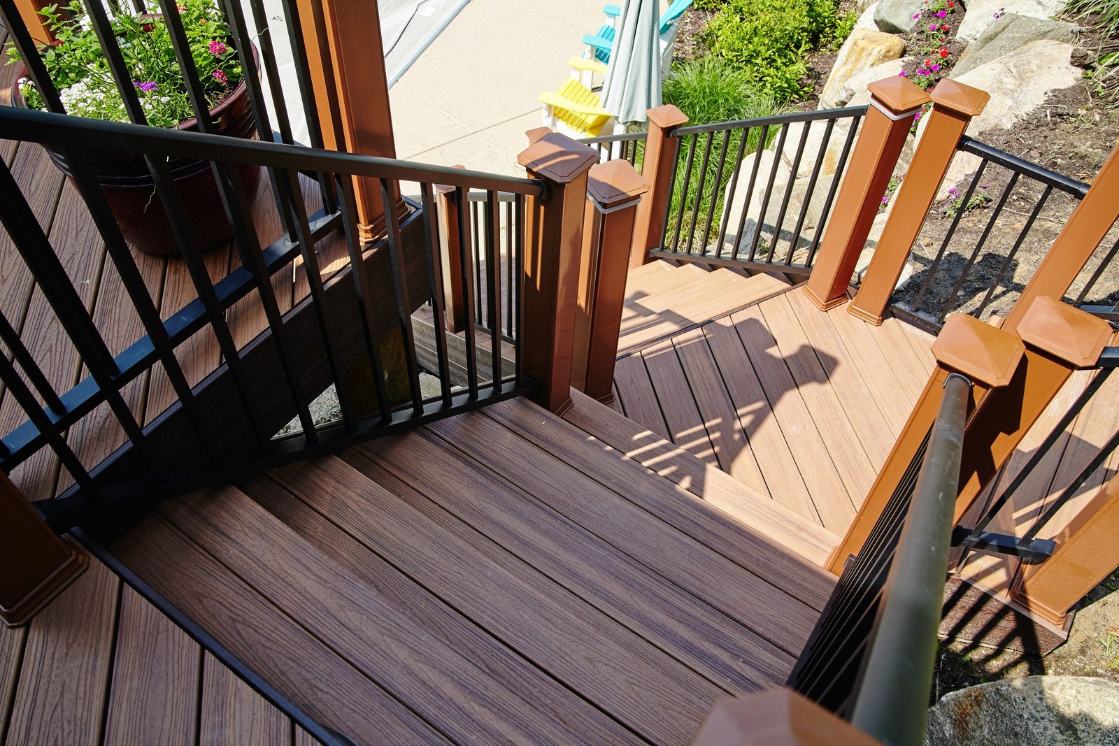 Outdoor wooden staircase with black railing, brown posts, and visible shadow.