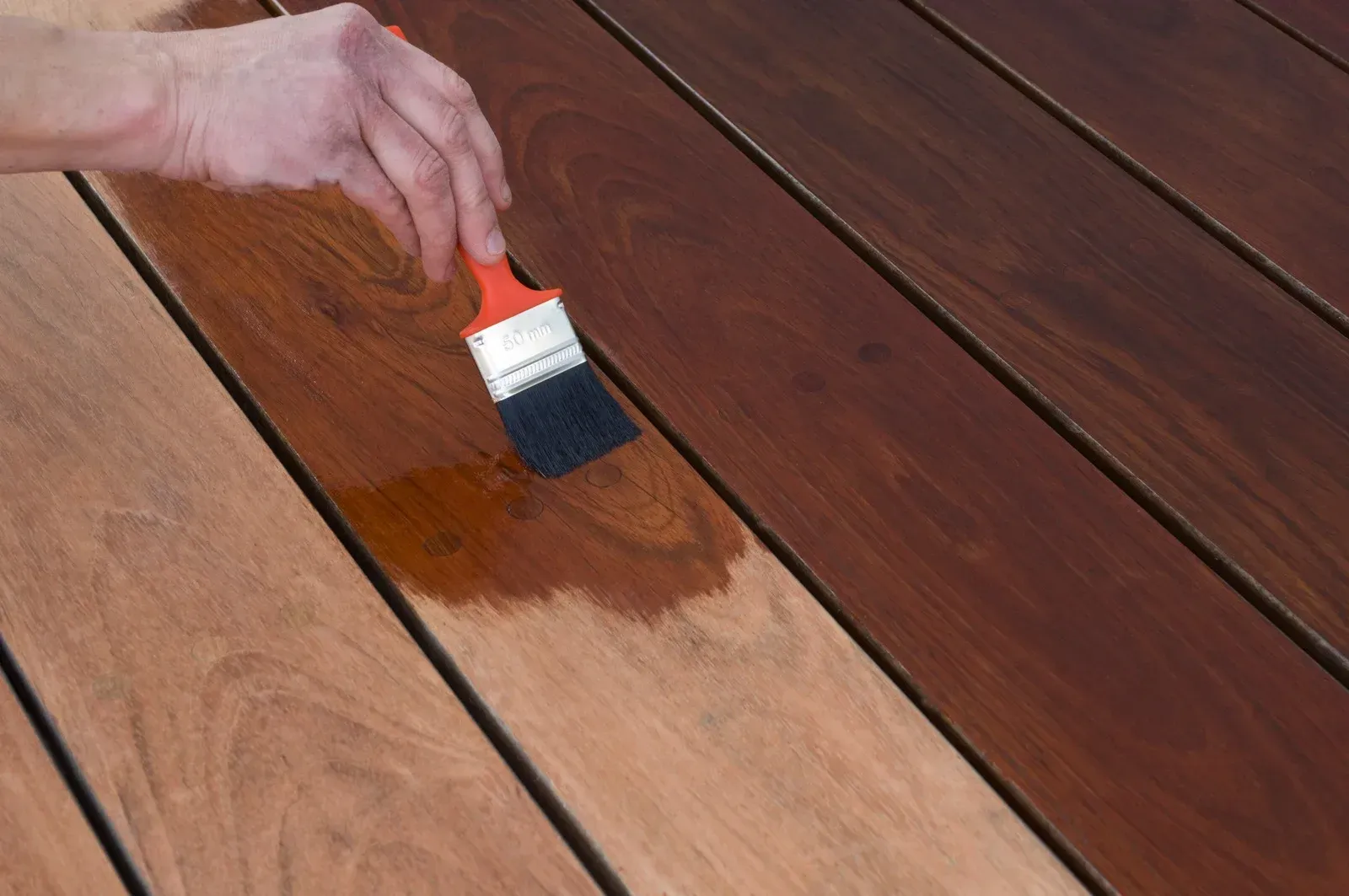 Hand staining wooden deck boards with a brush, creating a rich brown color.