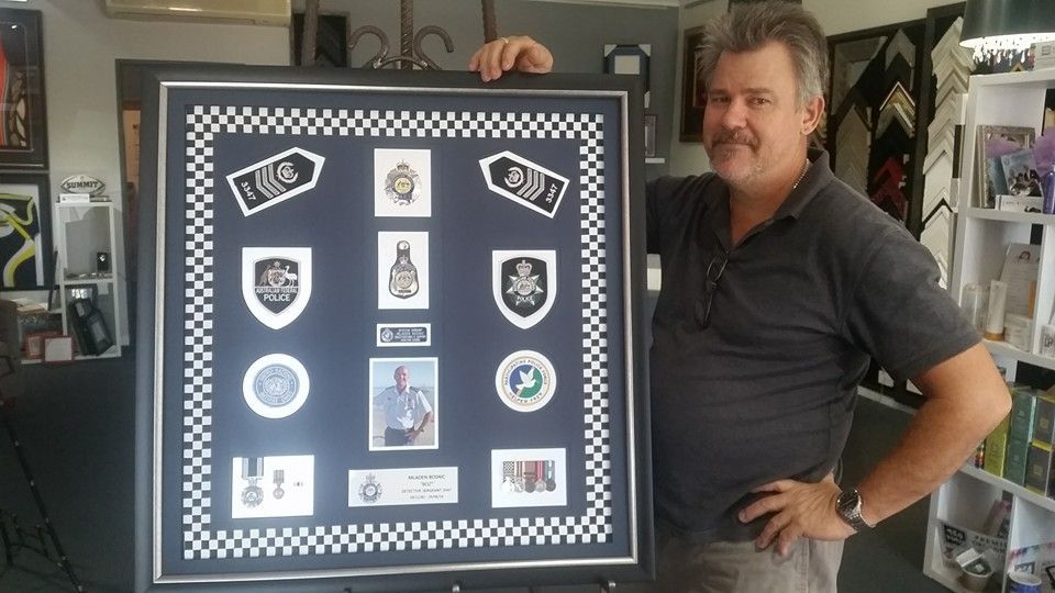 Man Holding Framed Police Badges, Shoulder Boards, and Photos — Tropical North Framing Gallery Cairns in Cairns, QLD