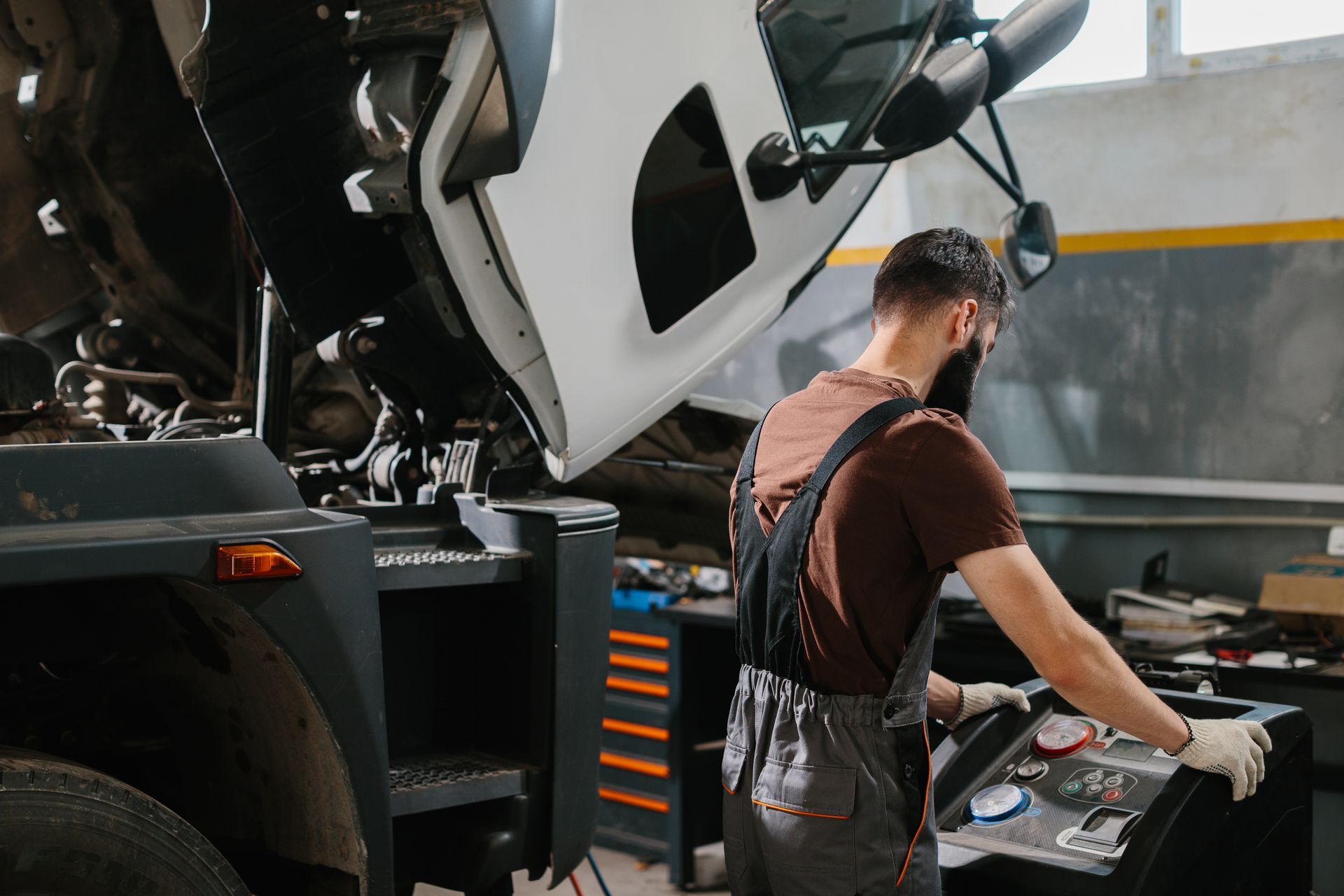 Mechanic working on a truck in a garage, using a diagnostic tool.