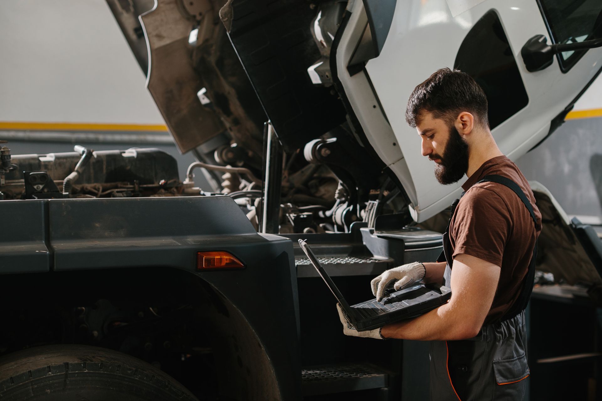 Mechanic using laptop to diagnose vehicle with hood open in a repair shop. Mechanic using laptop to diagnose vehicle with hood open in a repair shop.
