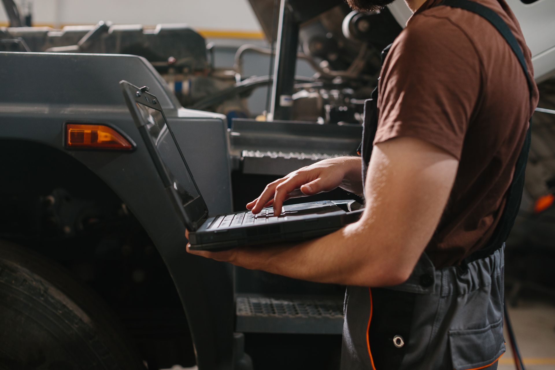 Mechanic uses laptop to diagnose vehicle engine in a garage.