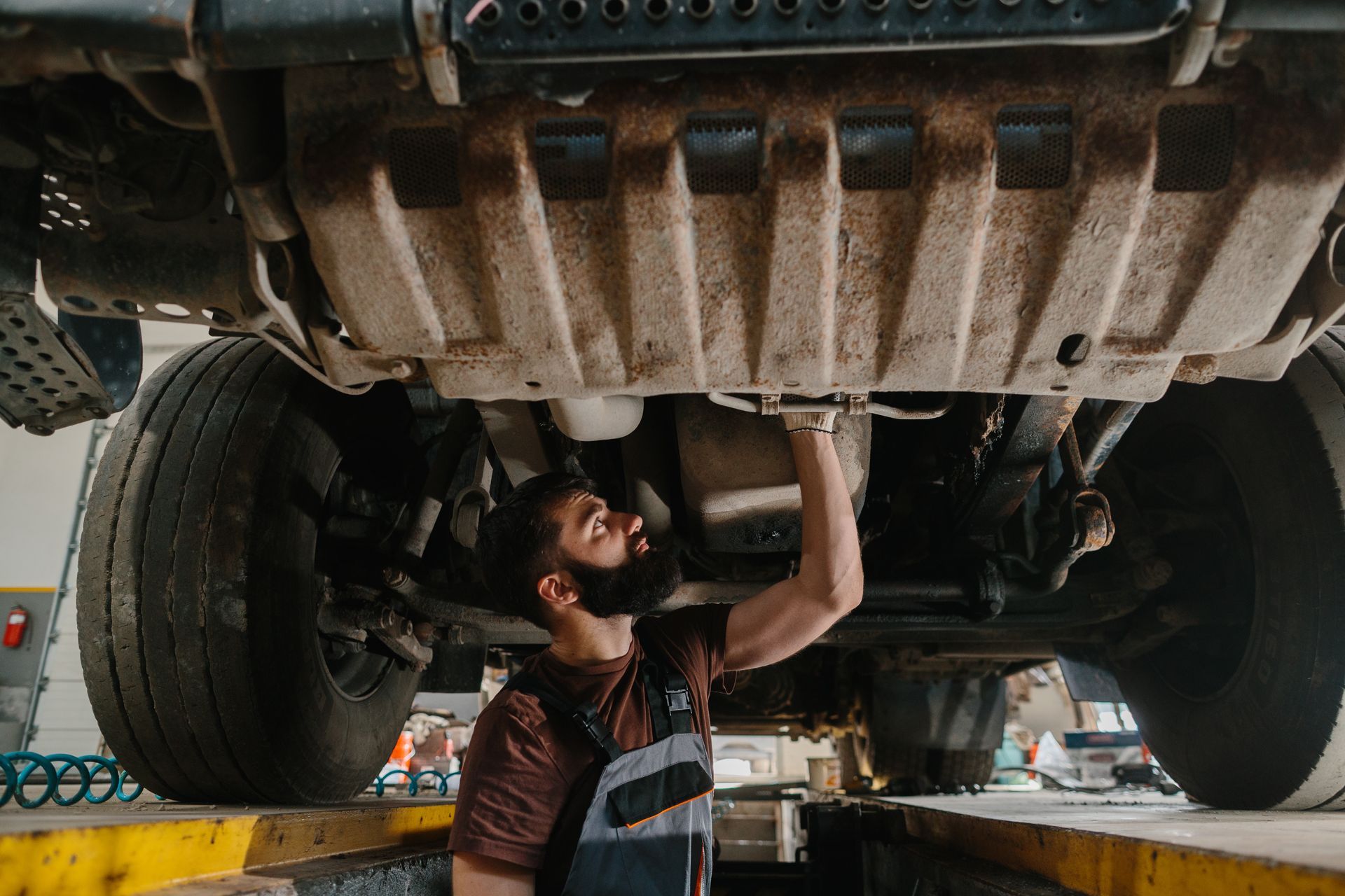 Mechanic inspecting undercarriage of vehicle in garage.
