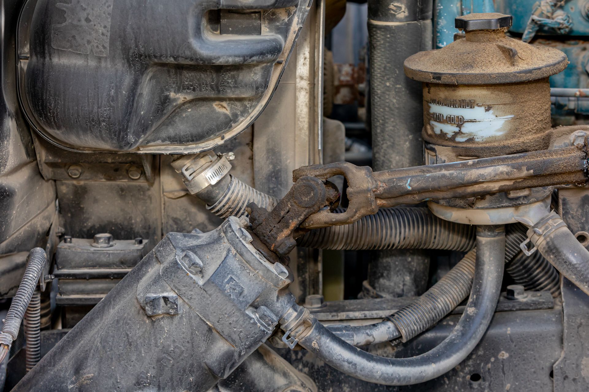 Close-up of a dirty, weathered engine with various pipes, tubes, and a round reservoir covered in grime.