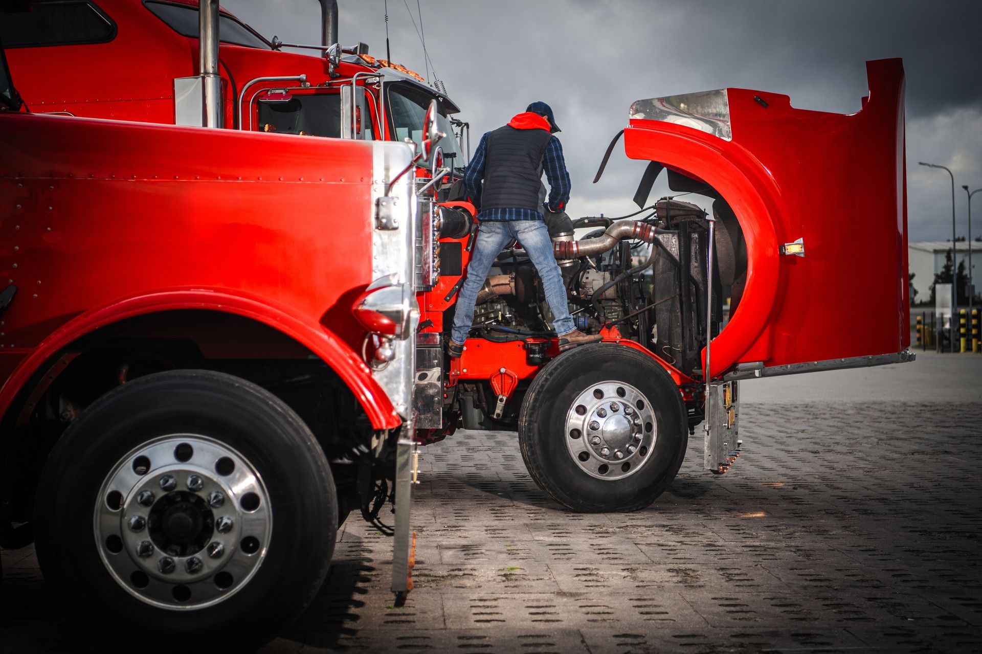 Mechanic in red and black clothes working on a bright red semi-truck engine.