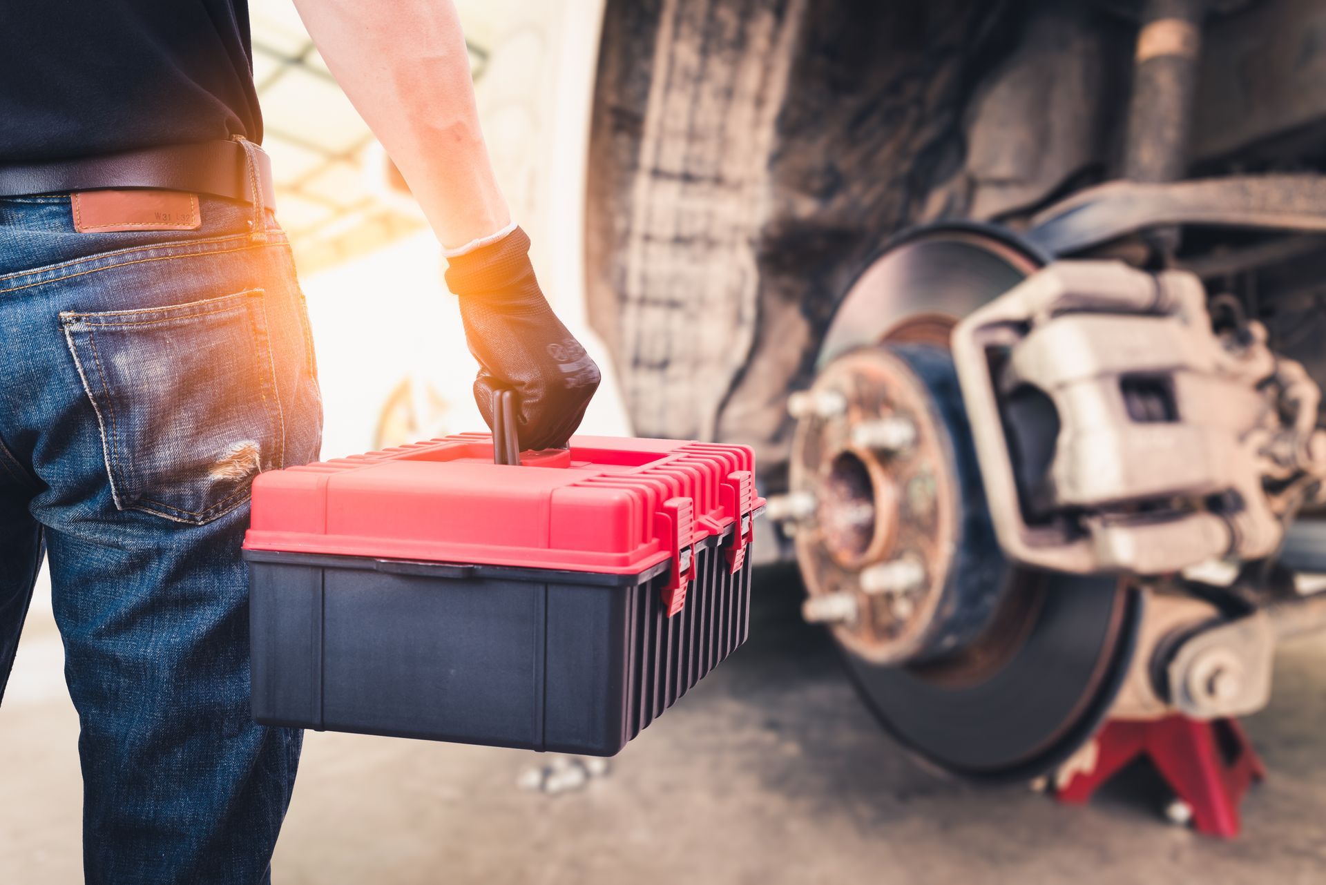 Mechanic holding toolbox near a car's brake system, ready to work.