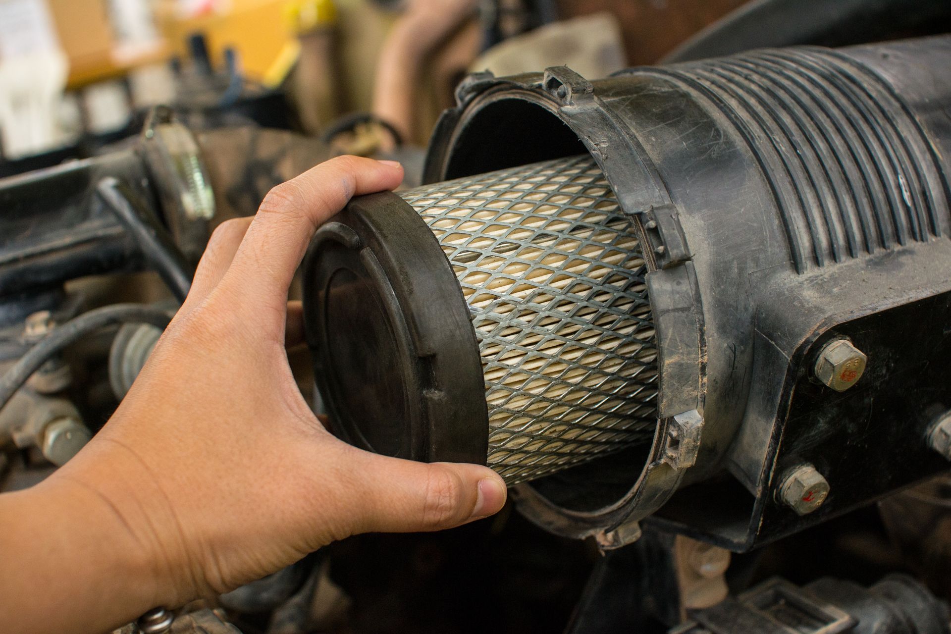 Hand removing a dirty air filter from a black air filter housing in an engine bay.