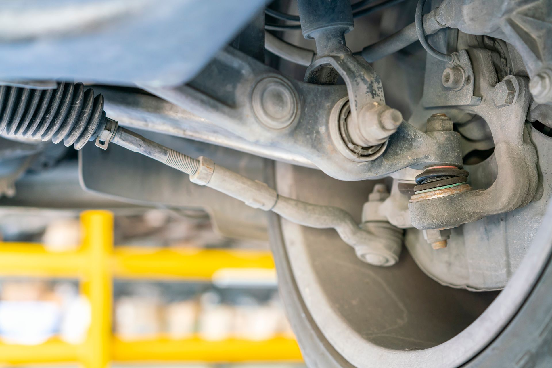 Close-up of a car's suspension and steering components, including tie rod and ball joint, in a garage setting. Close-up of a car's suspension and steering components, including tie rod and ball joint, in a garage setting.