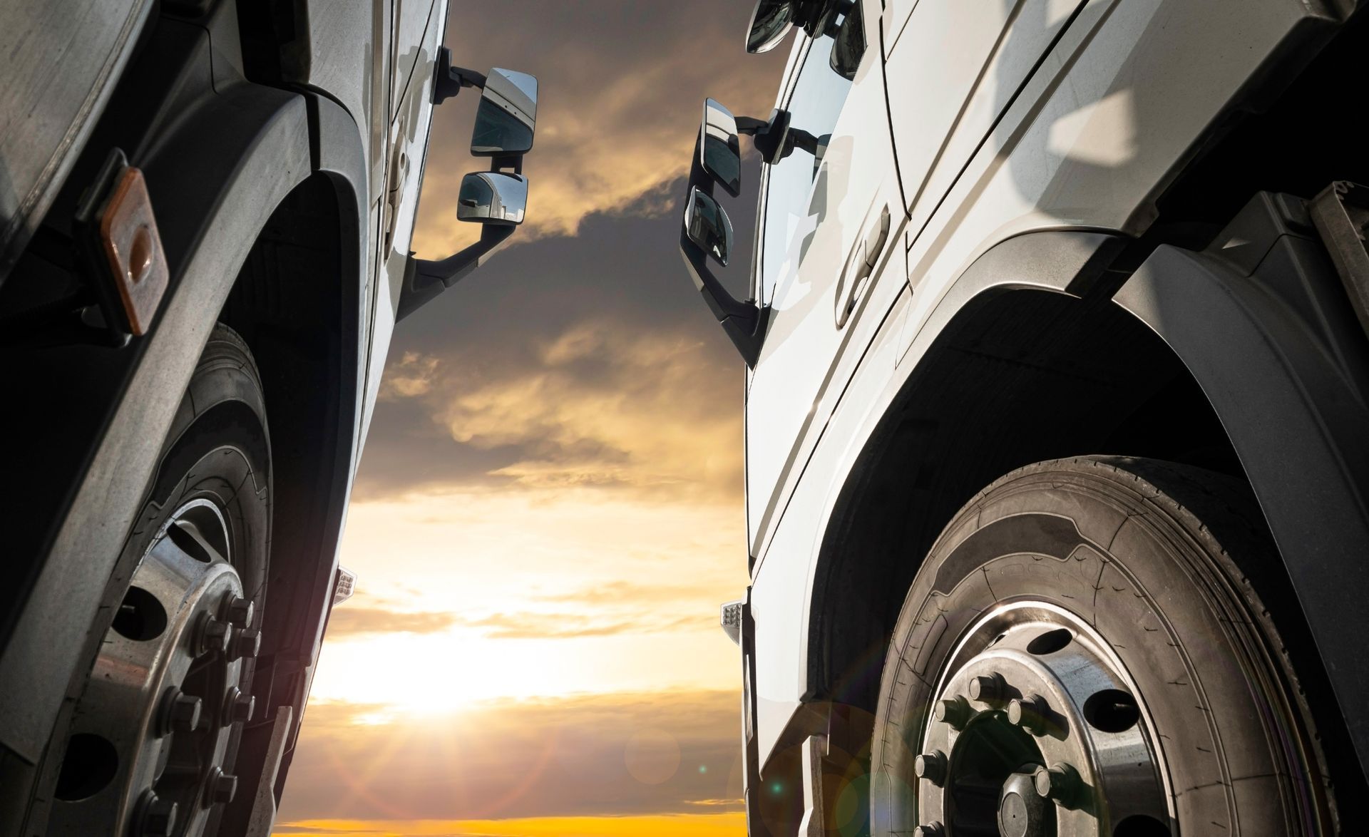 Two semi-trucks, wheels and fenders close up, facing each other against a sunset sky.