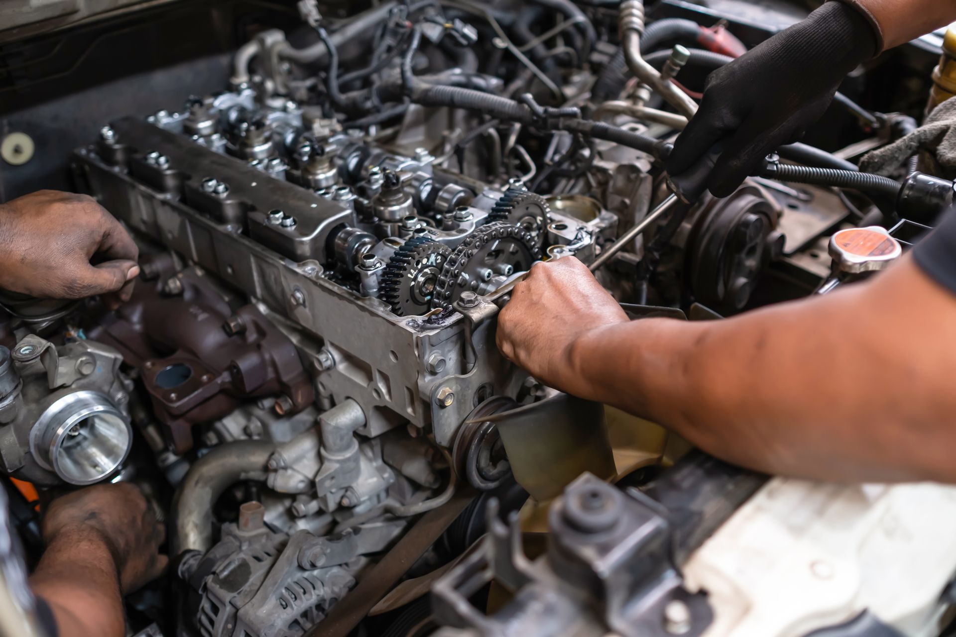 Mechanics working on a car engine, hands visible, inside a garage.