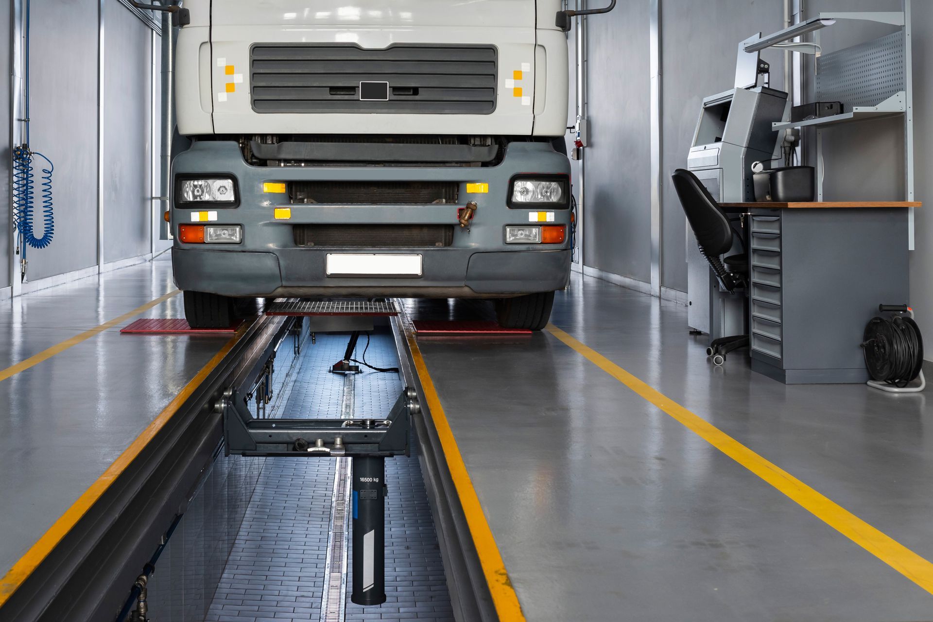 Truck inside an inspection bay, positioned over an inspection pit. Yellow lines mark the floor.