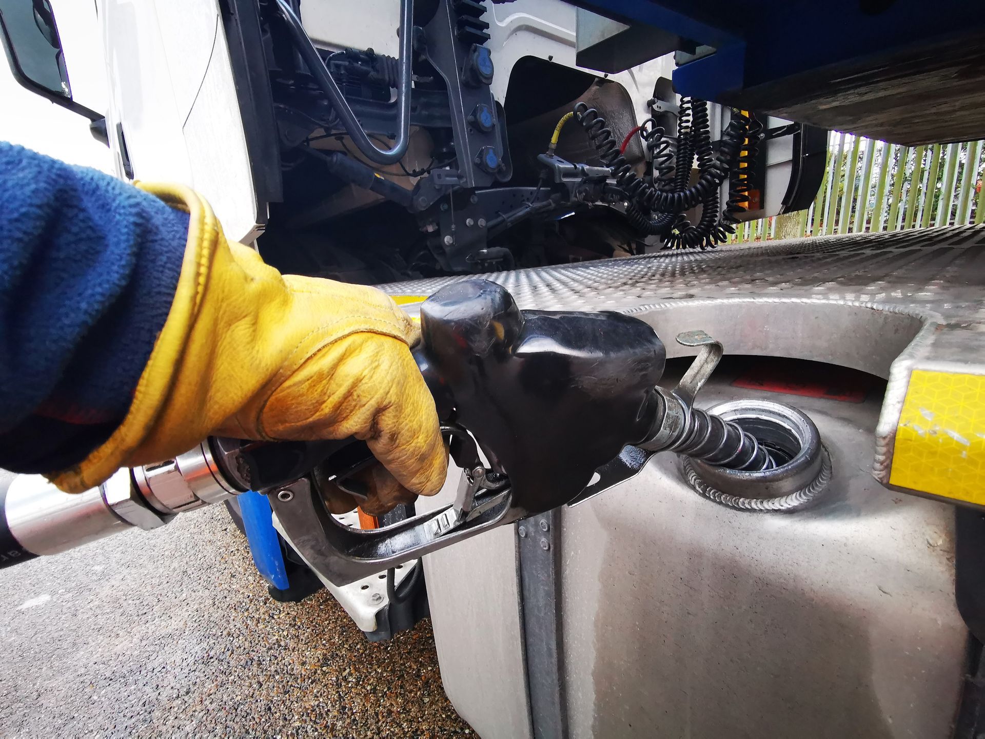 Hand in yellow glove fueling truck with black nozzle.