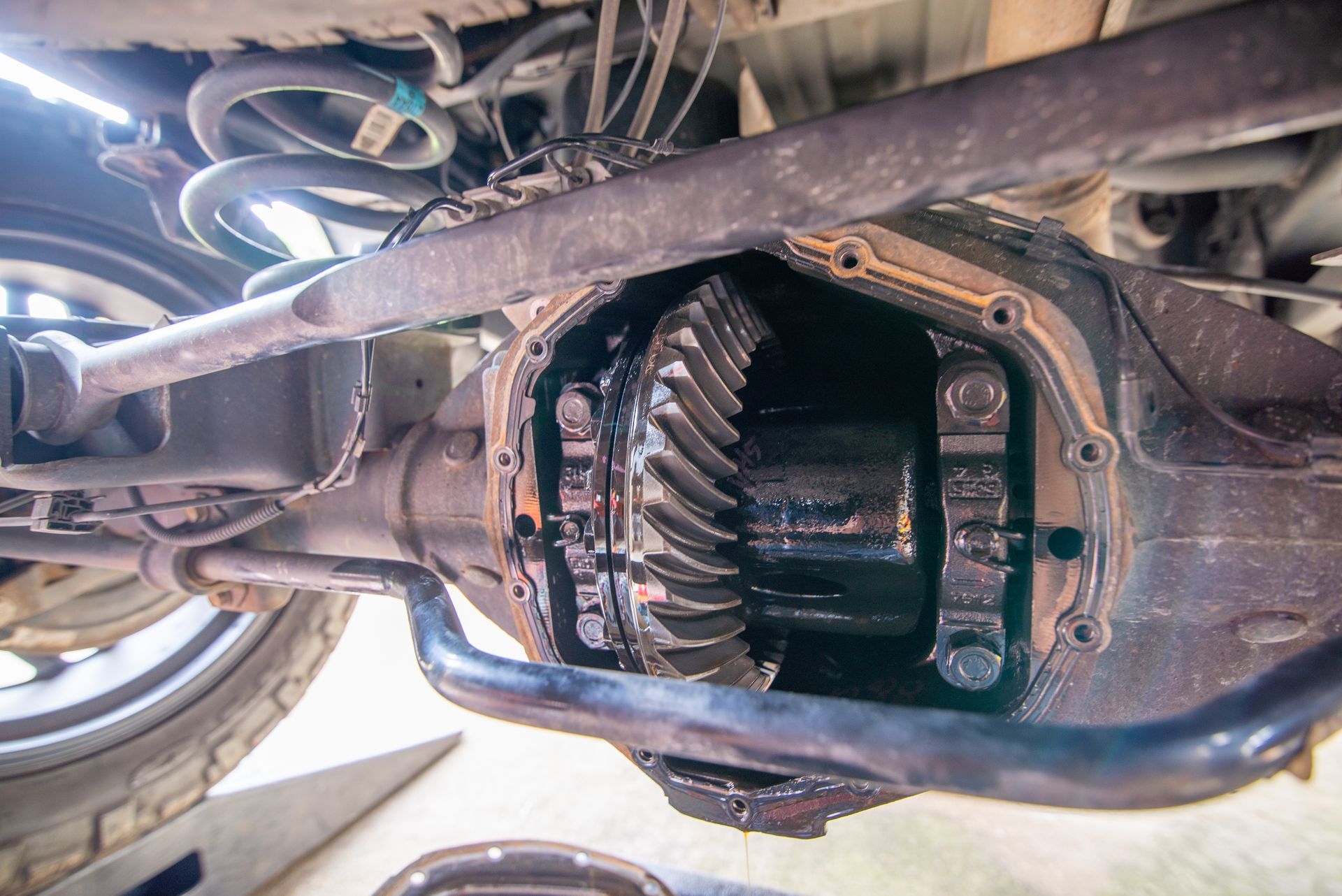 Rear axle differential with visible gears and oil, viewed from below.