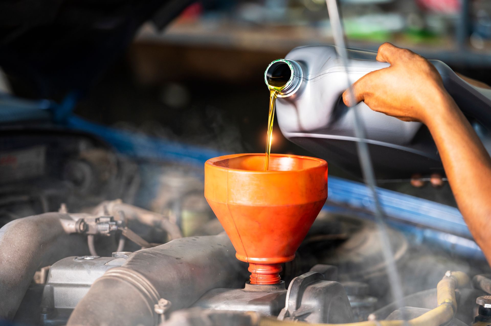 Person pouring oil from a container into a car engine using a funnel.